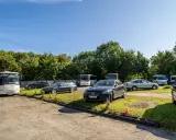 Na parkingu przy zamku Bolków stoi kilka samochodów i autobusów.