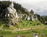 Malownicze **dolinki krakowskie** z wapiennymi skałami, lasami i rozbitymi namiotami. Ludzie spacerują i odpoczywają na trawie.