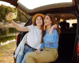 Dwie przyjaciółki robią sobie selfie nad jeziorem, ciesząc się wspólnym weekendem.