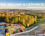 Widok z lotu ptaka na park zdrojowy w Ciężkowicach z placem zabaw, basenem i drewnianymi altanami.