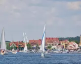 Żaglówki na jeziorze przed malowniczymi mazury miasta z czerwonymi dachami i wieżą kościelną.