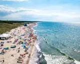 Tłum ludzi na plaży w Darłowie, korzystających z uroków lata. Wiele kolorowych parawanów i namiotów, a w wodzie kąpielowicze. To idealne darłowo atrakcje dla każdego.