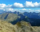 Widok na skaliste pasmo górskie, gdzie każdy zawrat szczyt zapiera dech. Błękitne niebo z białymi chmurami nad ostrymi grzbietami.