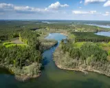 Malownicze pojezierze brodnickie jeziora otoczone gęstymi lasami, z błękitnym niebem i białymi chmurami w tle.