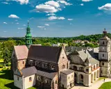 Wąchock atrakcje: Opactwo Cystersów z zieloną wieżą i wieżą zegarową na tle błękitnego nieba z chmurami.