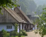 Drewniane domy w skansenie pomorskim, kryte gontem, stoją w rzędzie na tle zielonych wzgórz.