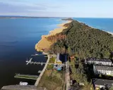 Dąbki atrakcje: malowniczy widok na jezioro, las, plażę i budynki. Widoczne molo, przystań jachtowa i zabudowania.