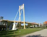 Żółty most pieszy, molo w Giżycku, z charakterystycznymi pylonami i linami, prowadzi do budynków nad jeziorem.