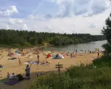 Tłoczna plaża nad jeziorem trzciańskim. Ludzie opalają się, kąpią i odpoczywają na piasku.