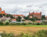 Widok na miasteczko z ceglanymi zamkami i kościołami, otoczone zielenią. W oddali pola uprawne. Wspaniałe **atrakcje** czekają na odkrycie!