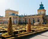 Barokowy pałac z żółtą fasadą i zielonym dachem, otoczony geometrycznym ogrodem. Wnętrze pałacu zachwyca bogactwem zdobień.