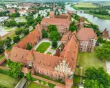 Malbork, największy zamek w Polsce, rozciąga się wzdłuż rzeki Nogat. Jego ceglane mury i liczne wieże tworzą imponujący krajobraz.