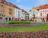 Kolorowy rynek w najstarszym mieście w Polsce, z kwitnącymi rabatami kwiatowymi i kamienicami.