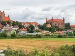 Widok na miasteczko z ceglanymi zamkami i kościołami, otoczone zielenią. W oddali pola uprawne. Wspaniałe **atrakcje** czekają na odkrycie!