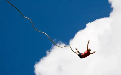Osoba skacze na bungee, doświadczając jednych z najbardziej ekstremalnych atrakcji w Polsce. Wolny lot na tle błękitnego nieba i chmur.