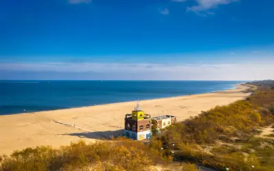 Piękna plaża i morze, idealne na spacer po urokliwych **miejscowościach nad morzem koło Gdańska**. W oddali widać charakterystyczny budynek.