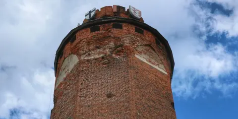 Wieża zamku krzyżackiego w Brodnicy, z cegły, z herbami na szczycie, na tle błękitnego nieba z chmurami.