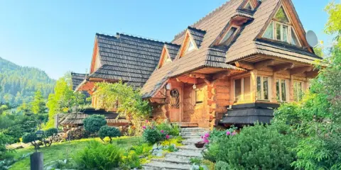 Piękny, drewniany domek w górach z dala od cywilizacji, otoczony zielenią i kwiatami.