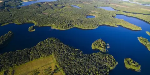 Malownicze jeziora na Mazurach otoczone gęstymi lasami, z widokiem na pola i dalsze akweny.