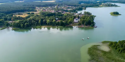 Malownicze jezioro Niesłysz z widokiem na wieś, lasy i dwa żaglówki na wodzie.