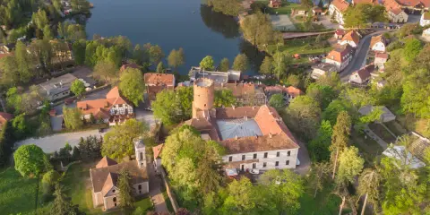 Malowniczy zamek i jezioro, idealne na wycieczki jednodniowe lubuskie. Wiosenna zieleń otacza zabytkowe budowle i spokojną taflę wody.