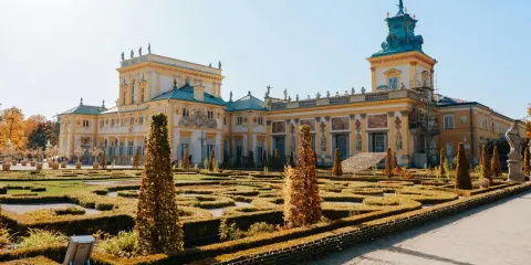Barokowy pałac z żółtą fasadą i zielonym dachem, otoczony geometrycznym ogrodem. Wnętrze pałacu zachwyca bogactwem zdobień.