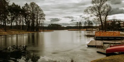 Zimowy krajobraz nad jeziorem w Rucianem Nidzie. Lodowa tafla, drewniane pomosty i czerwona łódka czekają na wiosnę.