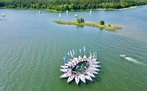 Żaglówki tworzą okrąg na jeziorze, idealne atrakcje Warmia i Mazury. W tle las i mała wyspa.