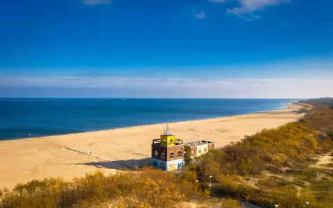 Piękna plaża i morze, idealne na spacer po urokliwych **miejscowościach nad morzem koło Gdańska**. W oddali widać charakterystyczny budynek.