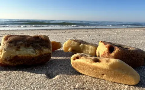 Kilka kawałków bursztynu leży na piaszczystej plaży, w tle widać spokojne morze i błękitne niebo.