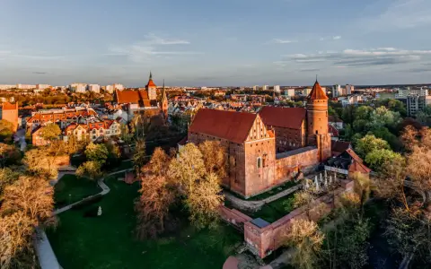 Zachód słońca nad zamkami na Mazurach. Czerwone dachy i ceglane mury w blasku złotej godziny.