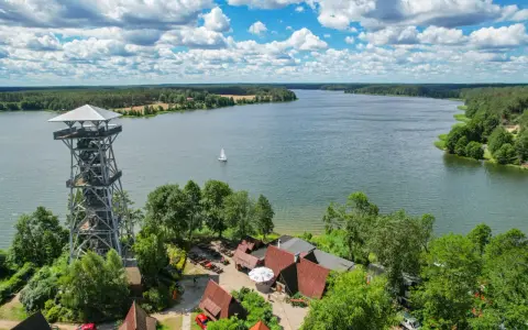 Wieża widokowa nad jeziorem, w tle las i żaglówka. Wdzydze Kiszewskie zapraszają do podziwiania piękna natury.