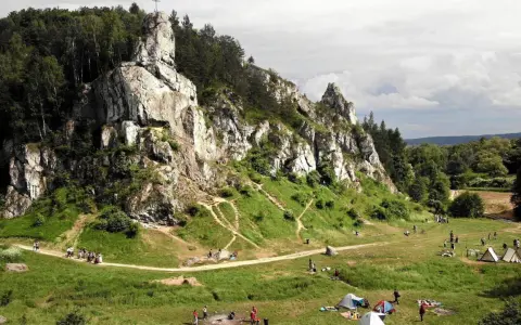Malownicze **dolinki krakowskie** z wapiennymi skałami, lasami i rozbitymi namiotami. Ludzie spacerują i odpoczywają na trawie.