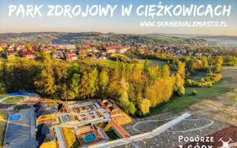Widok z lotu ptaka na park zdrojowy w Ciężkowicach z placem zabaw, basenem i drewnianymi altanami.