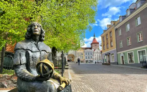 Pomnik Kopernika, jedna z głównych atrakcji Olsztyna, na tle kolorowych kamienic i błękitnego nieba.