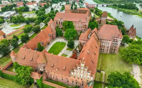 Malbork, największy zamek w Polsce, rozciąga się wzdłuż rzeki Nogat. Jego ceglane mury i liczne wieże tworzą imponujący krajobraz.