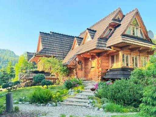 Piękny, drewniany domek w górach z dala od cywilizacji, otoczony zielenią i kwiatami.