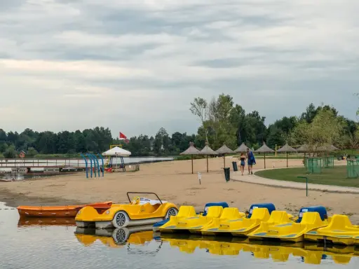 Plaża z żółtymi rowerami wodnymi i łódkami, idealna na weekendowy wypad na Mazury blisko Warszawy.