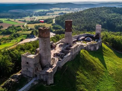 Zamek w Górach Świętokrzyskich, majestatycznie wznoszący się na wzgórzu, otoczony zielenią i malowniczym krajobrazem.