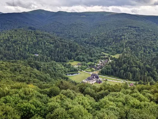 Widok z tarasu widokowego Bieszczady na zieloną dolinę z jeziorem i zabudowaniami.