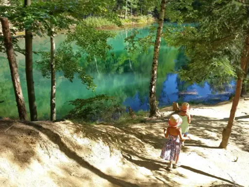 Dwie dziewczynki w słomkowych kapeluszach idą ścieżką w stronę turkusowego jeziora.