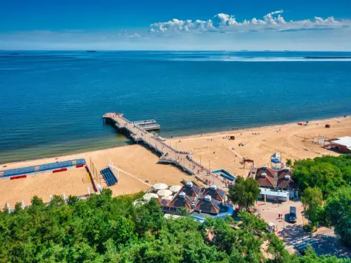 Idealne miejsce, gdzie na wakacje w sierpniu: piaszczysta plaża, molo, morze i zielone drzewa.