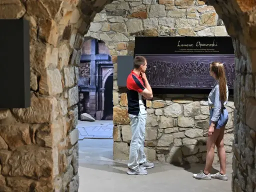 Zwiedzający podziwiają fragment nagrobka "Lament Opatowski" w kamiennych murach.