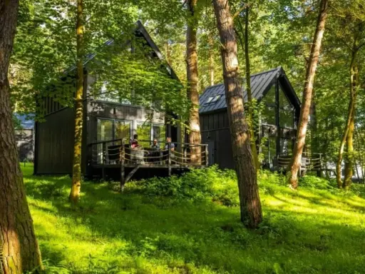 Nowoczesny hotel w lesie, z drewnianymi domkami i tarasem, otoczony zielenią.
