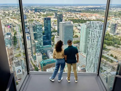 Para zwiedzająca Varso Tower taras widokowy, podziwia panoramę Warszawy.