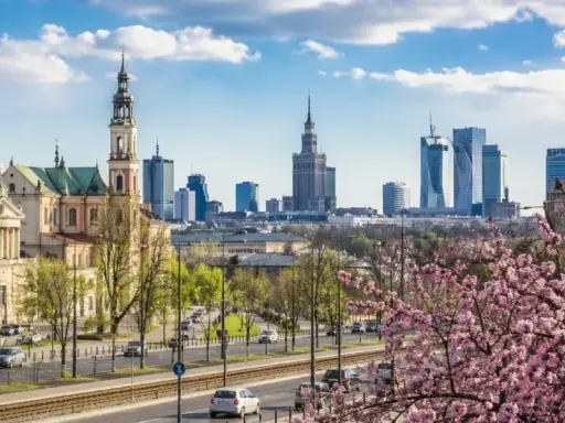 Majówka w Warszawie: zabytkowy kościół i nowoczesne wieżowce na tle kwitnącej wiśni.