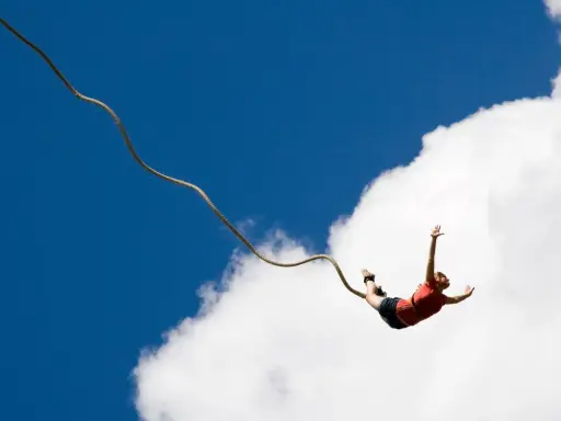 Osoba skacze na bungee, doświadczając jednych z najbardziej ekstremalnych atrakcji w Polsce. Wolny lot na tle błękitnego nieba i chmur.