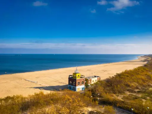 Piękna plaża i morze, idealne na spacer po urokliwych **miejscowościach nad morzem koło Gdańska**. W oddali widać charakterystyczny budynek.