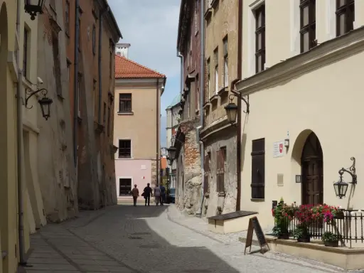 Wąska, brukowana uliczka w Lublinie z kamienicami i kilkoma spacerującymi osobami.