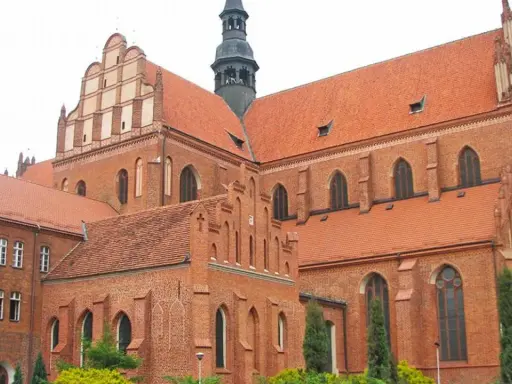 Majestatyczna pelplińska katedra z cegły, z charakterystycznymi dachami i wieżą, góruje nad otoczeniem.